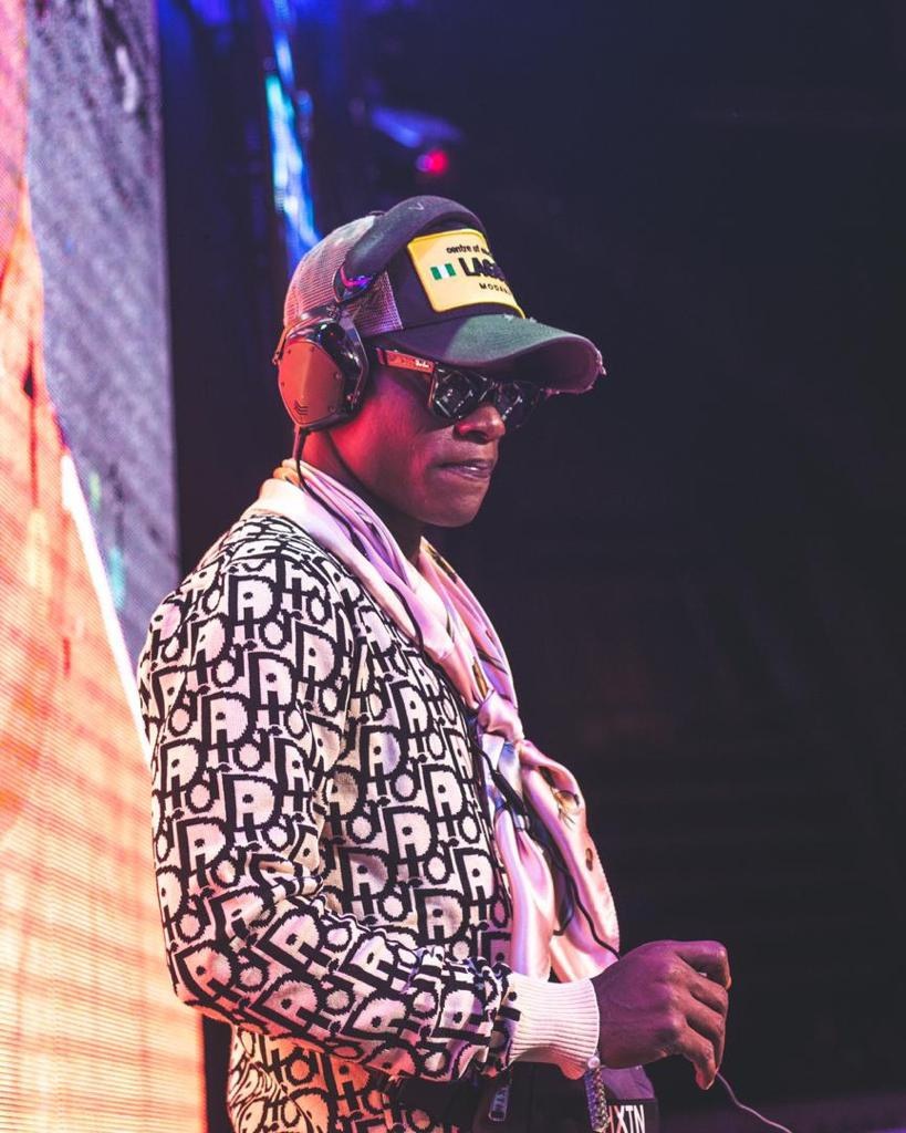 DJ Kenny performing live on stage in a patterned jacket